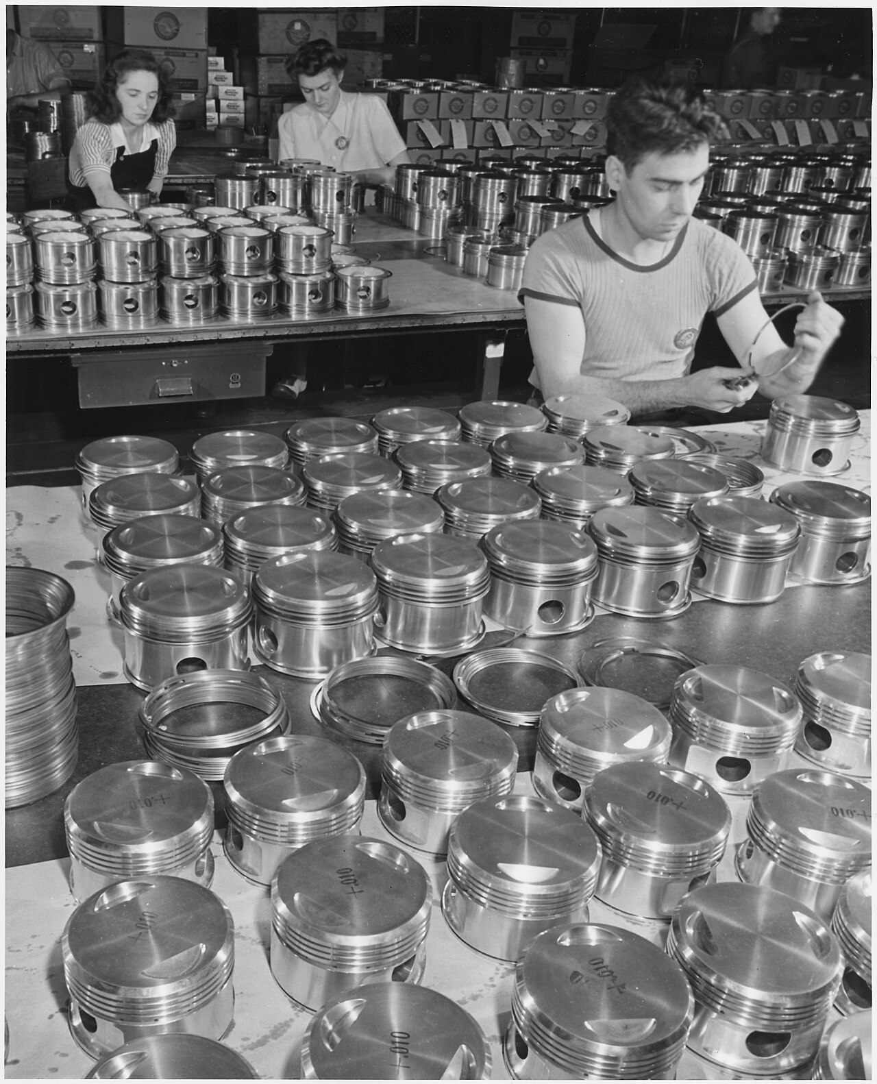 Workers fitting rings onto rows of Pratt and Whitney airplane-engine pistons in a large eastern plant, 1942.